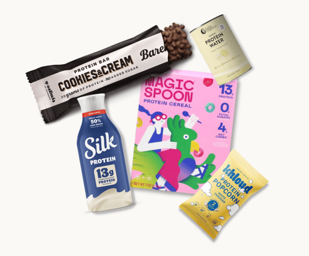 An assortment of high-protein snacks including a Bare protein bar, Silk protein drink, Magic Spoon protein cereal box, protein water can, and Khlowd protein popcorn bag.