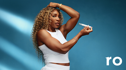 A strong athlete with curly hair wearing a white sleeveless top, holding a product in one hand and posing confidently against a blue background.
